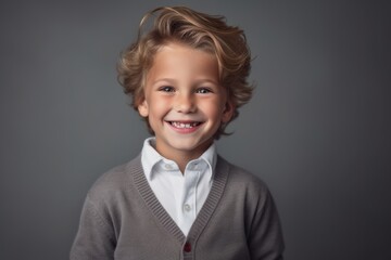 Portrait of a cute little boy with blond hair in a gray sweater on a gray background