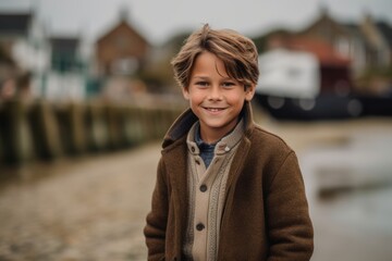 Fototapeta premium Portrait of a cute little boy in a brown coat on the beach
