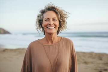 Fototapeta na wymiar Portrait of smiling mature woman standing on beach with hands in hair