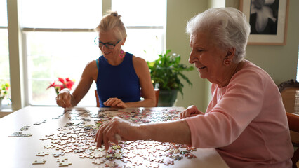 Happy smiling, laughing elderly senior woman sitting at table with mature middle aged daughter working on puzzle