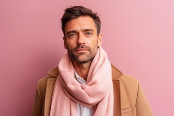 Obraz premium Handsome young man in coat and scarf looking at camera while standing against pink background