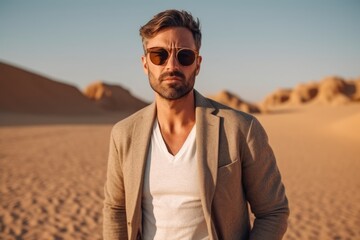 Handsome young man in sunglasses and jacket walking in the desert