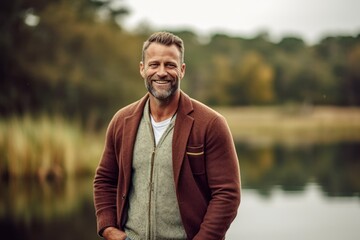 Obraz premium Handsome middle-aged man smiling and looking at camera while standing near a lake
