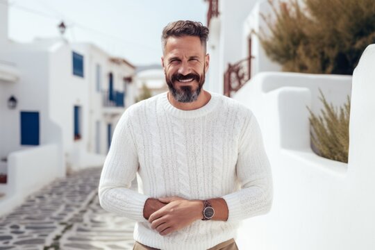 Cheerful mature man in white sweater standing with arms crossed and looking at camera