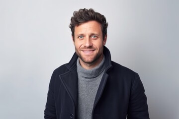 Obraz premium Portrait of a handsome young man wearing a coat and smiling while standing against a grey background
