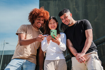 Young multicultural teenagers watching funny images on a smart phone. Three smiling young adult...