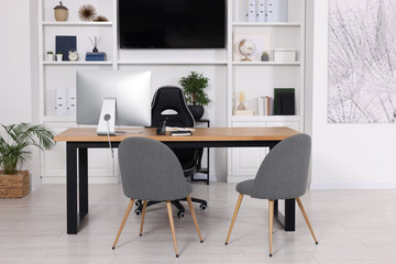 Stylish director's workplace with wooden table, tv zone, shelves and comfortable armchairs in room. Interior design