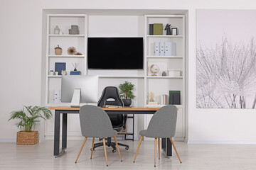 Fototapeta na wymiar Stylish director's workplace with wooden table, tv zone, shelves and comfortable armchairs in room. Interior design