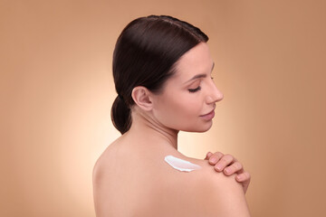 Beautiful woman with smear of body cream on her shoulder against light brown background