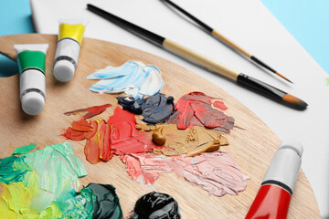Blank canvas, tubes of oil paints, brushes and palette on light blue background, closeup