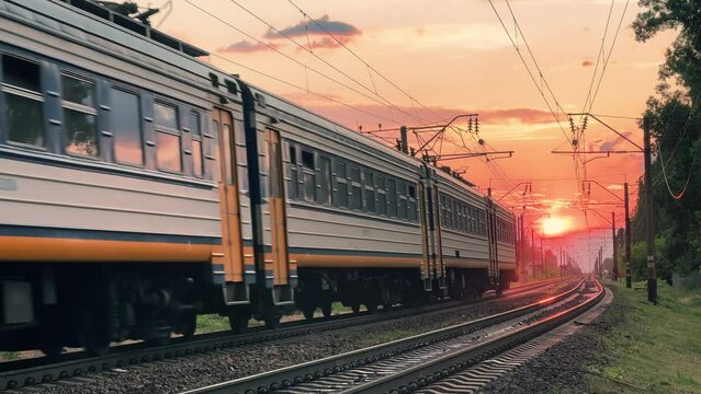 Suburban train travels through the countryside at a summer sunset. Front view. Long shot