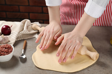 Woman rolling raw dough at grey table, closeup