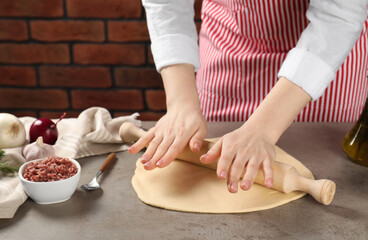 Obraz na płótnie Canvas Woman rolling raw dough at grey table, closeup