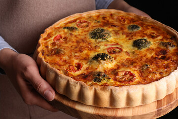 Woman holding delicious homemade vegetable quiche on black background, closeup