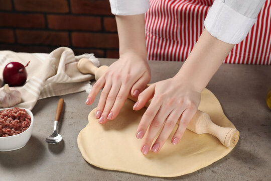 Woman rolling raw dough at grey table, closeup