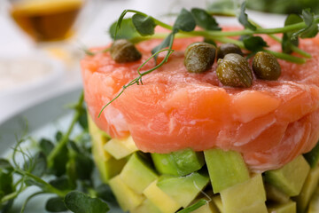 Tasty salmon tartare with avocado, capers and microgreens on plate, closeup