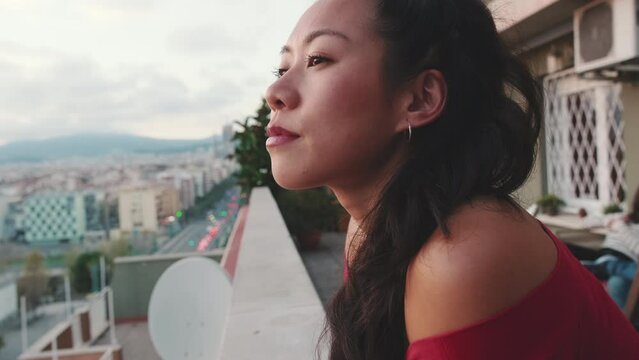 Close up, young woman standing on the balcony looking at the city at sunset