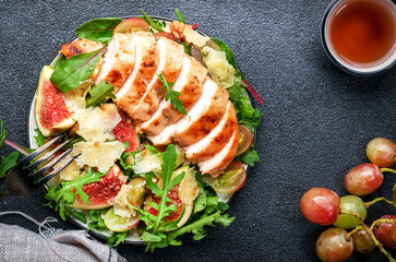 Gourmet salad with fresh figs, grilled chicken, parmesan cheese, grape, arugula, swiss chard with wine vinegar dressing. Black kitchen table background, top view