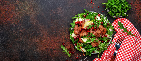 Tasty salad with pan-fried chicken liver, green apple, pomegranate and fresh arugula. Brown table...