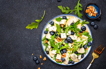 Gourmet salad with sweet pears, blueberries, blue cheese, arugula and walnuts. Black table background, top view