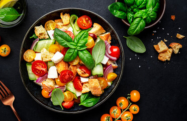 Panzanella salad with stale bread, colorful tomatoes, mozzarella cheese, onion, olive oil, salt and green basil, black table background, top view