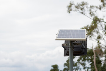 Photograph of a light pole with a solar panel and lamp, with a tree in the background and a cloudy...