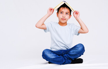 A thoughtful or dreaming boy, holding a book on his head, distracted from studying, highlighted on a white background.