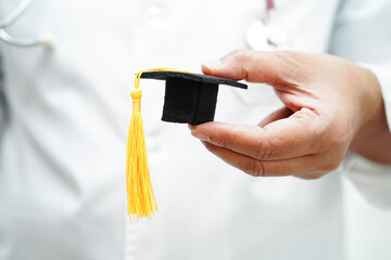 Asian woman doctor holding graduation hat in hospital, Medical education concept.
