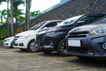 cars parked in a row in outdoor area of a mall car park have white, black, and grey color with palm trees and big stone wall