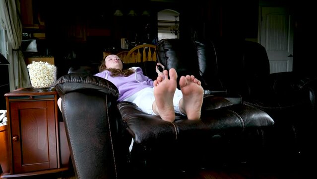 chic fashionable comfortable sofa teenage girl sits in chair and unfolds lying down in comfortable position in hands of remote control nearby popcorn waiting to watch movie close-up legs in frame