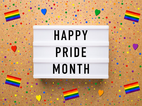 Lightbox on a wooden background with rainbow flags, hearts and confetti. Text on the lightbox: Happy Pride Month