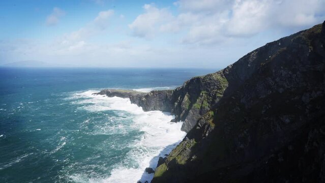 Slow motion blue ocean waves crashing at base of Irish cliffs
