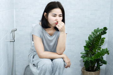 Asian Woman with Inflammatory Bowel Disease, Infections, Food Intolerances, and Allergies having bad Smelly Stools  sitting in a toilet - obrazy, fototapety, plakaty
