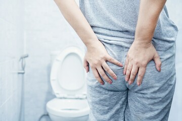 closeup of woman's hand holding butt due to hemorrhoid pain and discomfort in a toilet caused by...