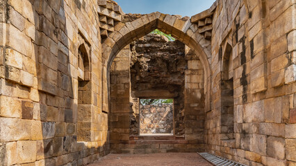 Ruins of the ancient temple complex Qutub Minar. A passage between weathered brick sandstone walls leads to the exit. The arch and the square opening are visible. Blue sky. India. Delhi.