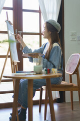 Fototapeta na wymiar Young female artist using paintbrush to drawing and painting masterpiece on canvas in home studio