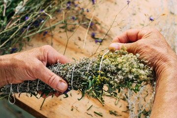 Women's hands tie bundle of medicinal herbs. Woman herbalist doctor prepares herbal collection, incense.