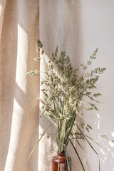 Aesthetic minimalist floral interior arrangement, green meadow grass in brown vase, sunlight rays...