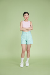 Full length of smiling young asian girl in casual clothes  holding hands crossed on pastel green background