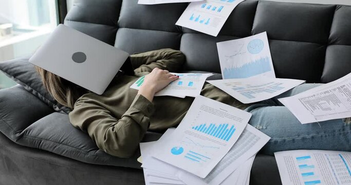 Tired woman sleeps on the couch with documents and laptop. Scattered document with text and graphics and tired freelancer