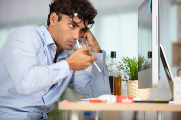 depressed businessman at desk drinking alcohol and holding a cigarette