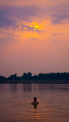 Silhouette of a guy in the water, with a vivid orange and pink sunset, Thakhek loop, Laos