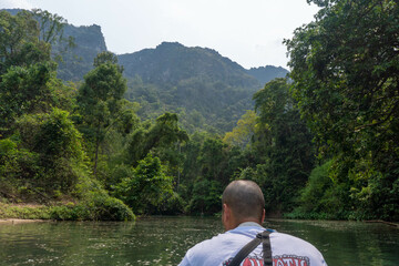 Short hair guy from behing in a canoe kayak on the lake of Kong lor cave, with green mountains in the background, Thakhek loop, Laos