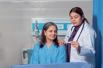 Indian female doctor using thermometer while check up to senior patient at hospital.