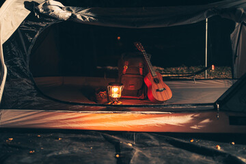 A gas lamp is on the tent floor at night and a bag with a ukulele and shoes next to it. Camping equipment, vocation and travel concept.