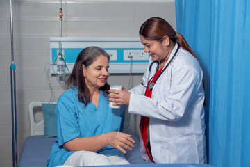 Indian female doctor giving glass of milk and helping to patient at hospital