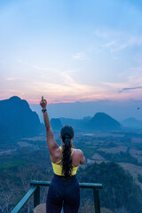 Brune latina girl on the top of a hill, looking at mountains during sunrise, in Vang Vieng, Laos