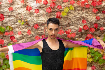 Portrait of biracial transgender man holding rainbow flag, with rocks and leaves in background