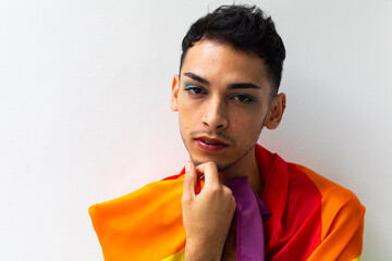 Portrait of biracial transgender man holding rainbow flag on white background