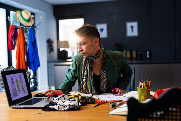 Biracial transgender fashion designer sitting at desk and using laptop